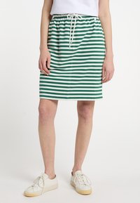 Grøn- og hvidstribet nederdel med elastisk talje og snøre, lavet af blødt stof, knælængde. Båret med hvide sneakers.