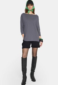 Szara bluzka z długim rękawem, czarne szorty, czarne buty do kolan i czapka w kolorze czarnym z zielono-różowym szalikiem zawiązanym wokół szyi.