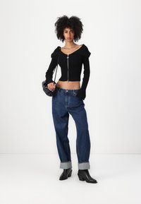Čierny rebrovaný crop top s off-shoulder dizajnom a strieborným zipsom. Skombinovaný s voľnými modrými džínami a čiernymi členkovými topánkami na podpätku.
