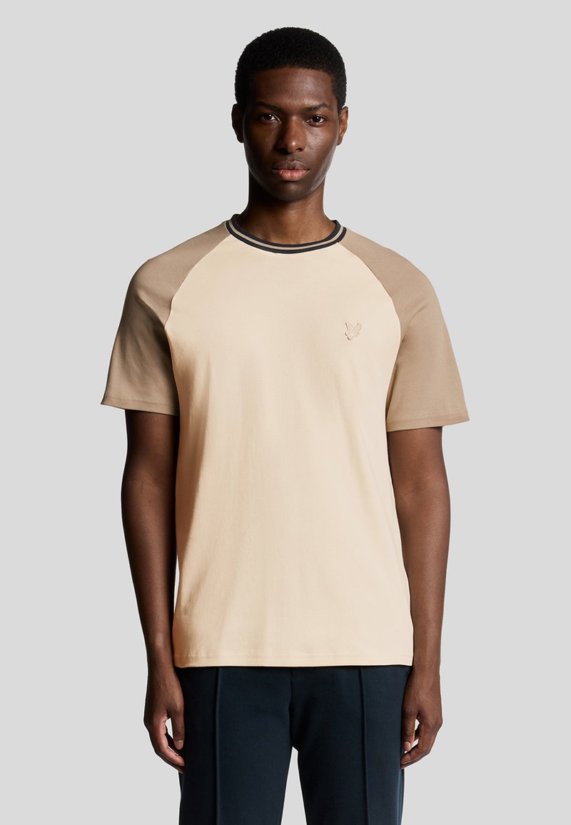 Kortærmet t-shirt lavet af blød bomuld, med en beige krop, taupe raglanærmer og en sort kantet halsudskæring med et lille logo.