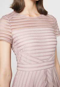 Jasnoróżowa sukienka z wyraźnym splotem z poziomymi i pionowymi paskami, krótkimi rękawami i dopasowanym gorsetem.