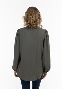 Olijfgroene blouse met gepofte mouwen, zachte stof, ronde zoom en elastische manchetten. Achteraanzicht toont eenvoud in ontwerp en kleur.