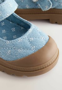 Scarpe in tessuto blu con un motivo floreale, puntale in gomma marrone e fascia in Velcro. La superficie testurizzata e la suola robusta offrono aderenza.