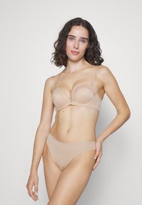 Soutien-gorge beige avec dentelle et bonnets rembourrés, accompagné d'une culotte bikini assortie en tissu lisse. Texture douce et légère.