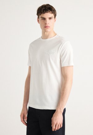 T-shirt en coton blanc avec un col rond, des manches courtes et un logo en relief sur la poitrine. Texture lisse et coupe standard.