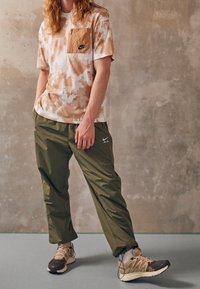 Kortärmad skjorta i ett tan- och vitprickigt mönster med en bröstficka, ihopparad med olivgröna byxor och beige sneakers.