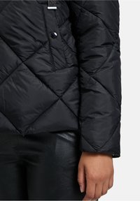 Sort dunjakke med quiltet struktur, skrå stikninger, trykknaplukning og en elegant finish. Matchet med sorte læderbukser.