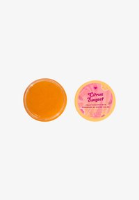 Scrub di zucchero all'acqua jelly in barattolo trasparente, riempito con un prodotto di un arancione vivace. Il coperchio rosa presenta il testo "Citrus Sunset" e dettagli grafici di frutti agrumi.