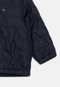 Navy Pufferjacke mit gestepptem Design, elastischen Bündchen und Saum. Mit einem Logo-Patch am Ärmel. Glatte, glänzende Material.