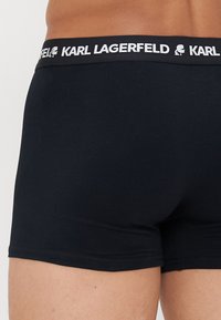 Fekete boxeralsó sima szövetből, széles derékkal, amelyen fehér "KARL LAGERFELD" logo található, minimális design, minta nélkül.