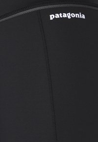 Czarne legginsy sportowe wykonane z elastycznego materiału, z płaskimi szwami; posiadają białe logo "Patagonia" na pasku.