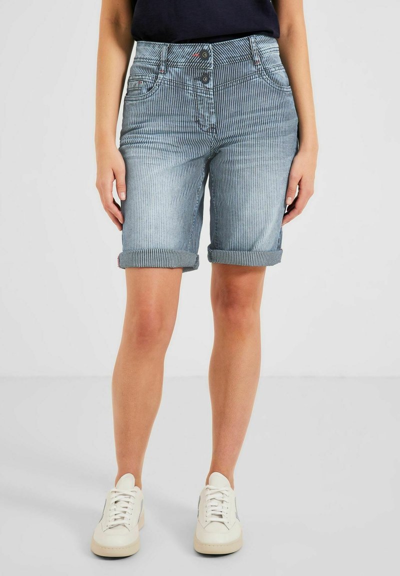 Ljusblå jeansshorts med randigt mönster, uppvikta fållar, tvåknappsförslutning och sidofickor, kombinerade med vita sneakers.