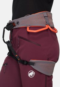Gros plan d'un pantalon d'escalade marron foncé avec un harnais rembourré gris et orange comportant des boucles pour mousquetons et des sangles réglables.