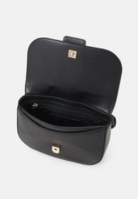 Borsa a mano in pelle nera con forma strutturata, hardware dorato, chiusura magnetica e interno a fantasia con tasca con zip.