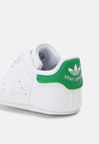 Witte leren sneaker met groene accenten. Bevat een geperforeerd ontwerp aan de zijkant en een gevoerde hiel. Tekst op de hiel leest "stan smith." Getextureerde zool.