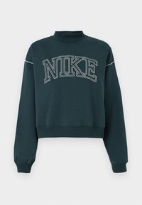 Tumši tīnī krāsā īsās piedurknes sporta krekls, izgatavots no mīksta auduma, ar augstu apkakli, ar lielu balto "NIKE" logo uz krūtīm.