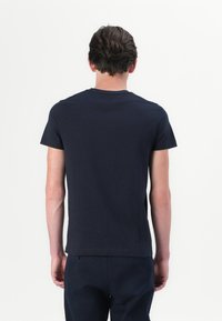 Camiseta de manga corta azul marino, fabricada en algodón. Presenta un cuello redondo y un diseño ajustado. Textura suave, sin patrones visibles.