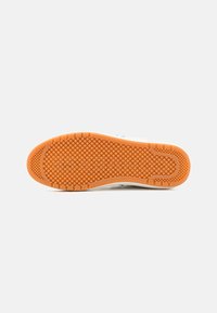 Semelle de chaussure avec grip en caoutchouc orange comportant des motifs de semelle circulaires et rectangulaires sur un fond blanc.