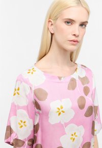 Kortærmet top i pink stof med store hvide blomster mønstre med gule accenter og brune blade, rund halsudskæring, glat tekstur.