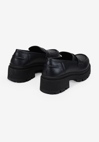 Zapatos de plataforma de cuero negro con punta redondeada, suela de goma gruesa y detalles de costura en la parte trasera. Diseño de talón cerrado.