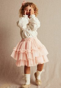 Rynket lyserød tyl nederdel med elastisk talje, parret med en hvid broderet skjorte med knaplukning og beige balletflade. Stribede sokker fuldender looket.