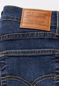 Spijkerbroek met een donkere blauwe wassing, oranje stiksel, achterzakken en een bruine leren patch met het gegraveerde opschrift "Levi Strauss & Co."