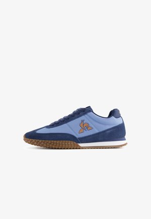 Zapatillas deportivas azules con parte superior de ante y sintético, suela de goma con agarre texturizado y un acento en naranja en el logo.