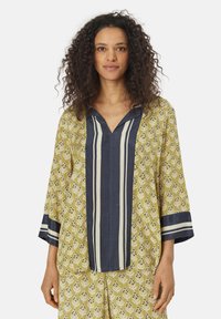 Maglietta lunga e morbida di colore verde oliva con un motivo floreale, dettagli in blu navy e righe a contrasto sul davanti.