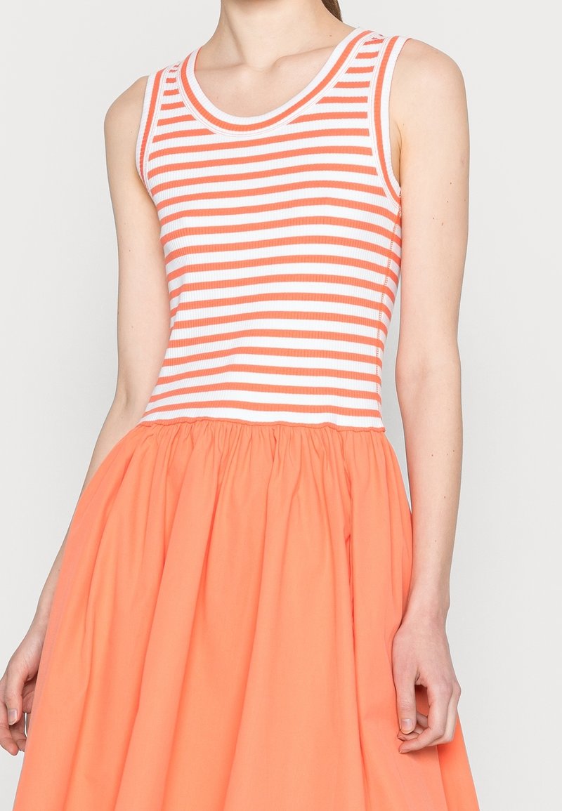 Débardeur rayé orange et blanc, associé à une jupe orange unie avec des plis. Le tissu semble léger et texturé.