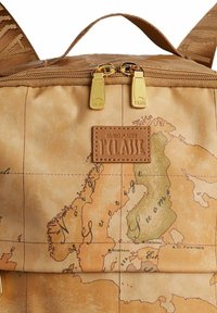 Mochila marrón con estampado de mapa, con cremalleras doradas y un parche de logo de cuero. El material tiene un acabado suave y texturizado.