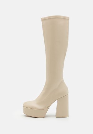 Botte beige à plateforme montant jusqu'au genou avec talon bloc épais et texture lisse, vue de côté sur fond blanc.
