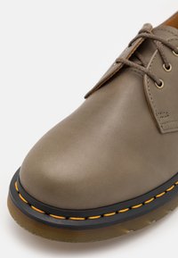 Gros plan d'une chaussure à lacets en cuir taupe avec une semelle noire ornée de coutures jaunes et une semelle extérieure brune translucide.