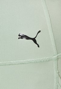 Top atletico verde chiaro realizzato in tessuto a coste, con logo Puma nero e dettagli di cucitura a contrasto.