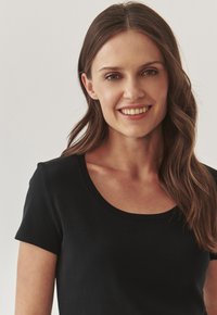 T-shirt noir à manches courtes avec un col rond, fabriqué en tissu doux, avec une texture lisse et une coupe ajustée.