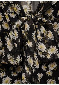 Tissu noir à motifs de marguerites blanches noué en un nœud lâche avec une texture visible et des centres de fleurs vert jaunâtre.