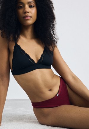 Zwarte bralette met kant afgebiesd, voorzien van driehoekige cups, gecombineerd met bordeauxrode slipjes met een logo-label aan de zijkant. Glad stofoppervlak.