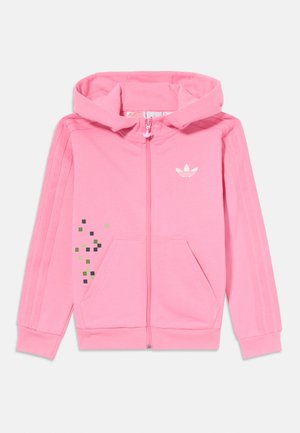 Roza zip-up majica s kapuljačom, prednjim džepovima i tri bijele pruge duž rukava. Sadrži pikselski uzorak u zelenoj i crnoj boji.