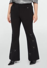 Black flared pants with a smooth texture, featuring silver embellishments arranged in star-like patterns, complemented by a high waistband and buttons.
