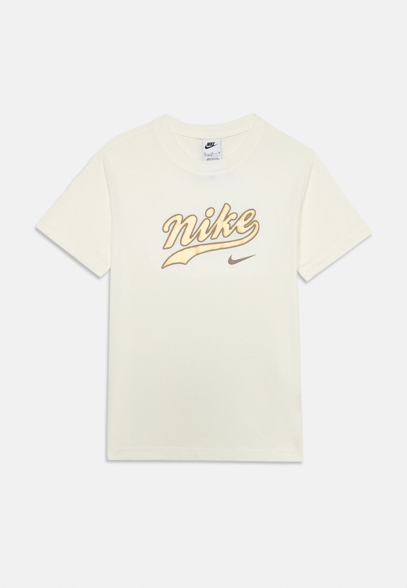 Krēmkrāsas kokvilnas t-krekls ar lielu zelta Nike logotipu un mazāku brūnu Swoosh logotipu. Īsām piedurknēm un apaļas kakla dizains.
