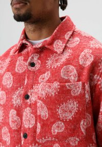 Rood flanellen overhemd met wit paisleymotief, voorzien van een puntige kraag, zwarte knopen en een borstzak. Gemaakt van een getextureerde wolmix.