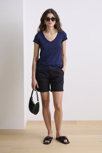 Jūras spēku V veida kakla t-krekls, melni šorti un melnas sandales. Aksesuāri ietver melnu rokassomu un saulesbrilles. Gluda auduma, ikdienas piegriezums.