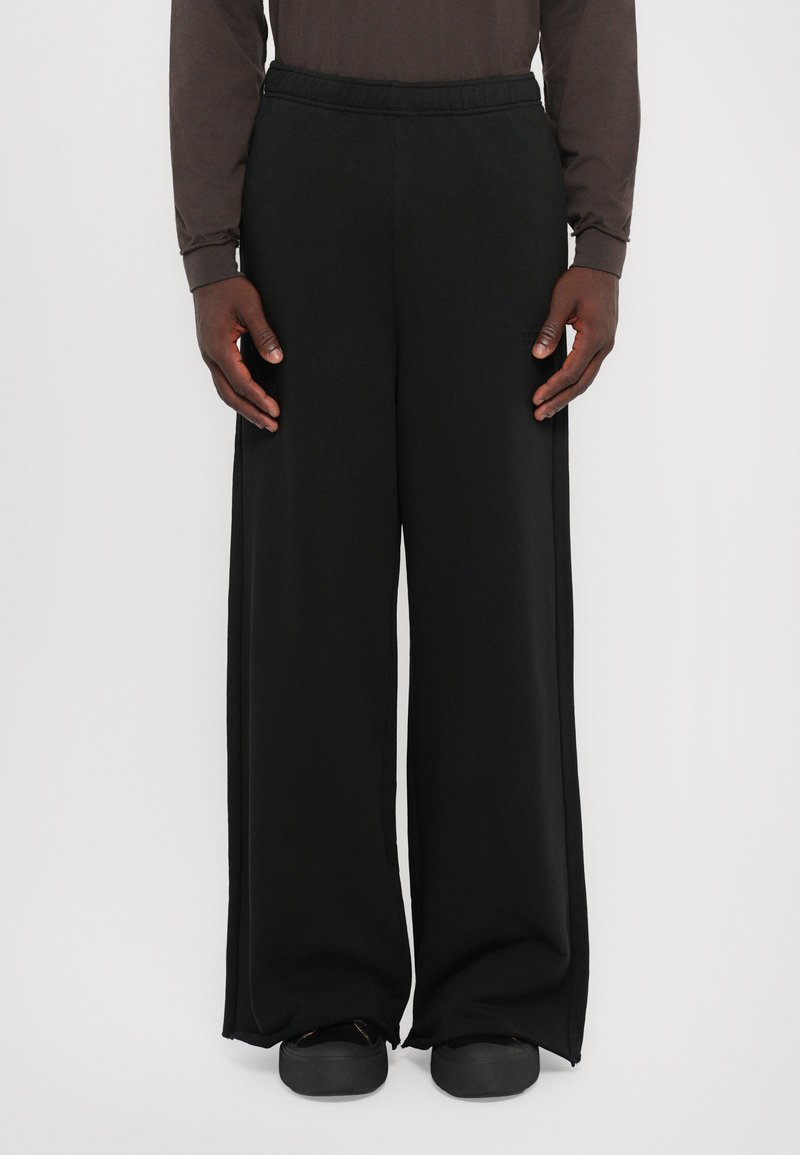 Black wide-leg pants with an elastic waistband, made from a smooth fabric. Features side seams and a loose fit, paired with black shoes.