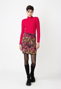 Rode geribbelde langesleeve coltrui, minirok met bloemenprint in roze, groen en zwart tinten. Model draagt zwarte kniehoge laarzen.