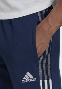 Navy athletic pants with white Adidas logo, featuring a side pocket and striped accents in a mesh texture. Soft, stretchy material.