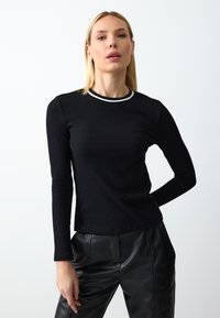 Schwarzes, geripptes Langarmtop mit Rundhalsausschnitt und weißen Akzenten. Der Stoff scheint weich zu sein und hat eine figurschmeichelnde Passform.