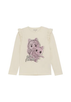 T-shirt crème à manches longues avec des détails sur les épaules volants, présentant un graphique d'une fille de dessin animé et d'un chat avec le texte "Meilleures Amies."