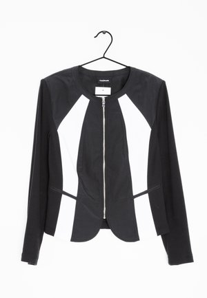 Chaqueta corta en blanco y negro hecha de tejido elástico, con cierre de cremallera en la parte delantera, cuello redondo y dos bolsillos frontales horizontales.