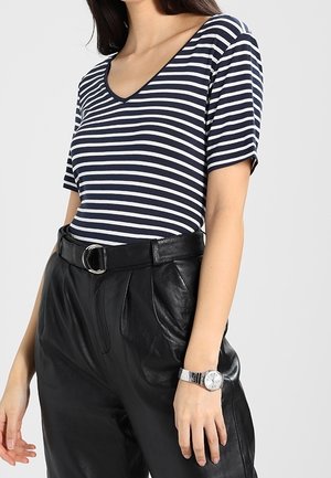 Kort mouwshirt met V-hals met marineblauwe en witte strepen, gecombineerd met hooggetailleerde zwarte leren broek. Zilveren horloge met een ronde kast om de pols.