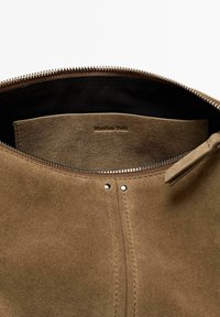 Sac en daim marron avec fermeture éclair argentée partiellement ouverte, montrant l'intérieur noir et le logo embossé "Massimo Dutti" à l'intérieur de la poche.