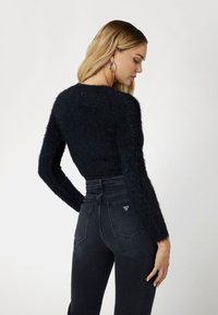 Black, fluffy, cropped sweater with long sleeves paired with high-waisted, dark gray jeans featuring a triangular logo detail on the back pocket.
